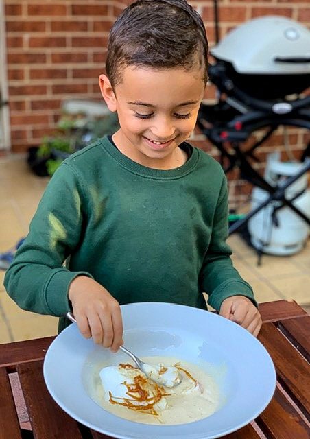 boy eating a bowl of ile flottante with vanilla sauce