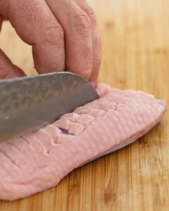Scored duck breast with sharp knife on wooden chopping board