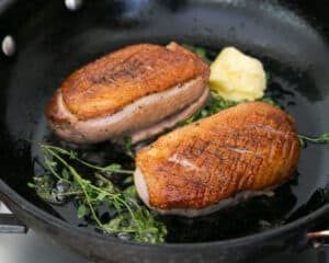 Pan fried duck breasts in an iron skillet with butter and thyme