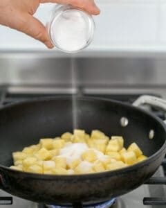 Sugar added to diced pineapple in a pan over flame