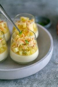 Panna cotta topped with pineapple dices, mint leaves and toasted coconut flakes in a dessert glass