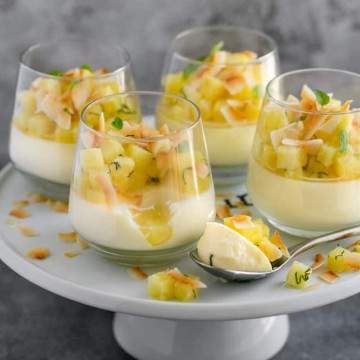 4 dessert glasses on top of a white cake stand with ready to eat pina colada panna cotta