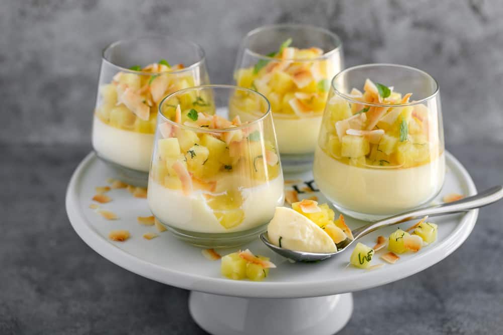 4 dessert glasses on top of a white cake stand with ready to eat pina colada panna cotta