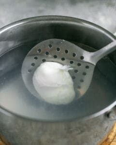 taking out a Poached egg with a slotted spoon from a pot of hot water