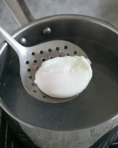 taking out a Poached egg with a slotted spoon from a pot of hot water