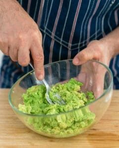 Crushing the avocado flesh with a fork in a glass bowl
