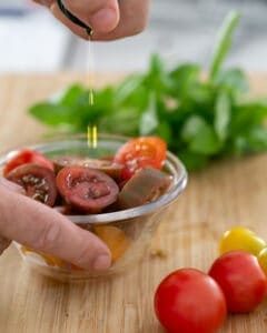 Chooped medley of tomatoes in a glass bowl being drizzled with olive oil