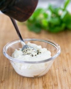 Seasoning ricotta cheese in a glass bowl with salt and pepper