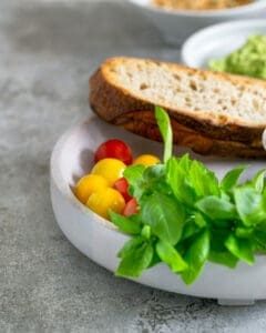 Basil leaves, medley of tomatoes, toasted sour dough in a white wooden bowl