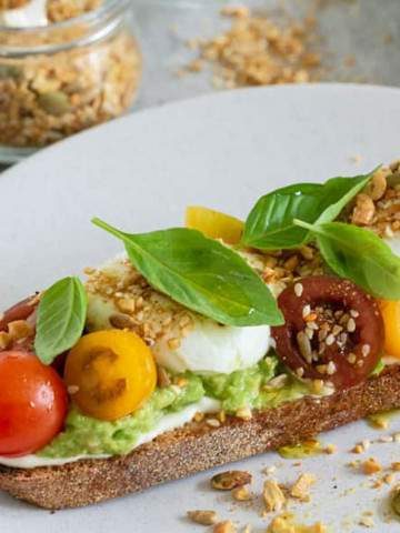 breakfast set up on table with Slice of sourdough with ricotta, crushed avocado, poached eggs, cherry tomatoes, basil and dukkah