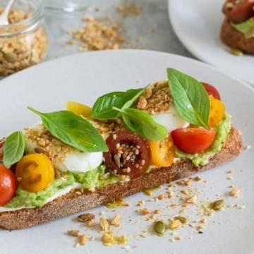 breakfast set up on table with Slice of sourdough with ricotta, crushed avocado, poached eggs, cherry tomatoes, basil and dukkah