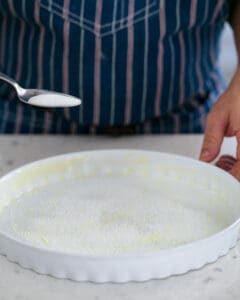 Spoon of sugar ready to be sprinkled on the greased baking dish