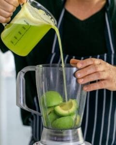 Apple and lime juice mix poured over cut avocados in a mixer