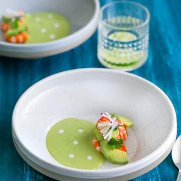 Overhead shot of Avocado soup in a bowl with fresh avocado slices, poached prawns, garnished with coriander and sliced radish