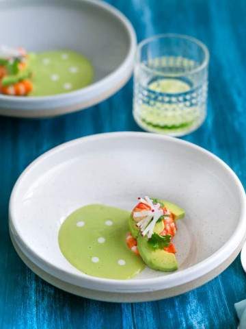 Overhead shot of Avocado soup in a bowl with fresh avocado slices, poached prawns, garnished with coriander and sliced radish