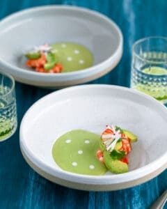 Overhead shot of Avocado soup in a bowl with fresh avocado slices, poached prawns, garnished with coriander and sliced radish