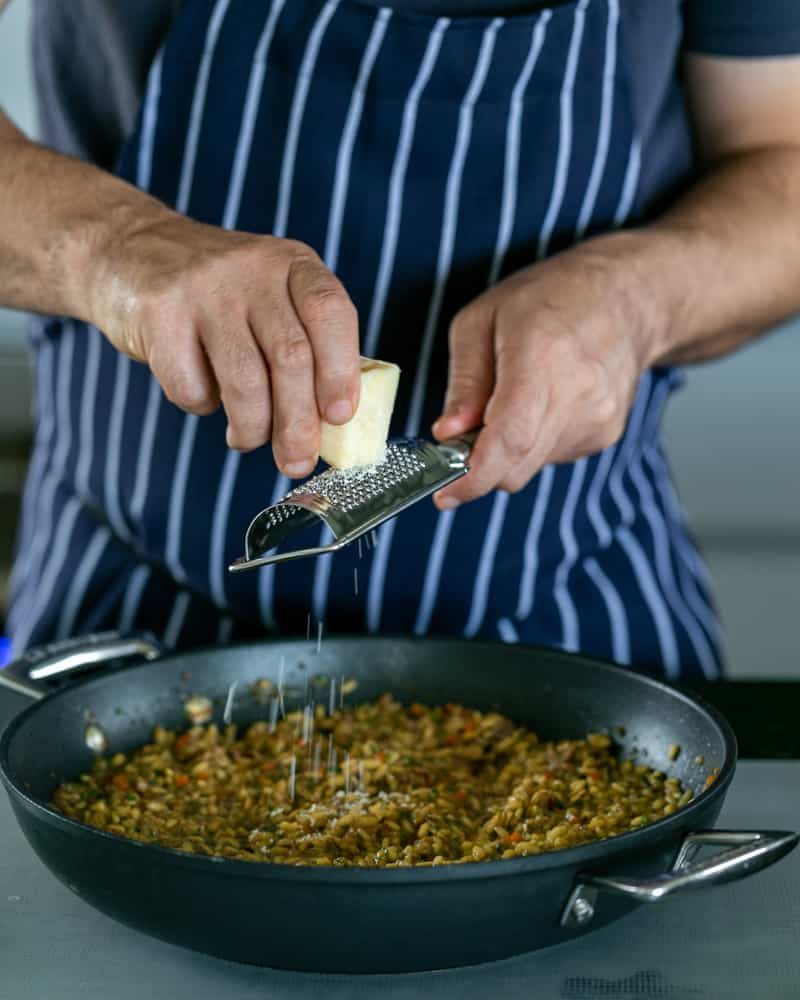 Grating Parmesan on cooked risotto in a pan