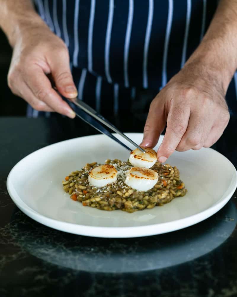 Arranging pan seared scallops on porcini mushroom risotto