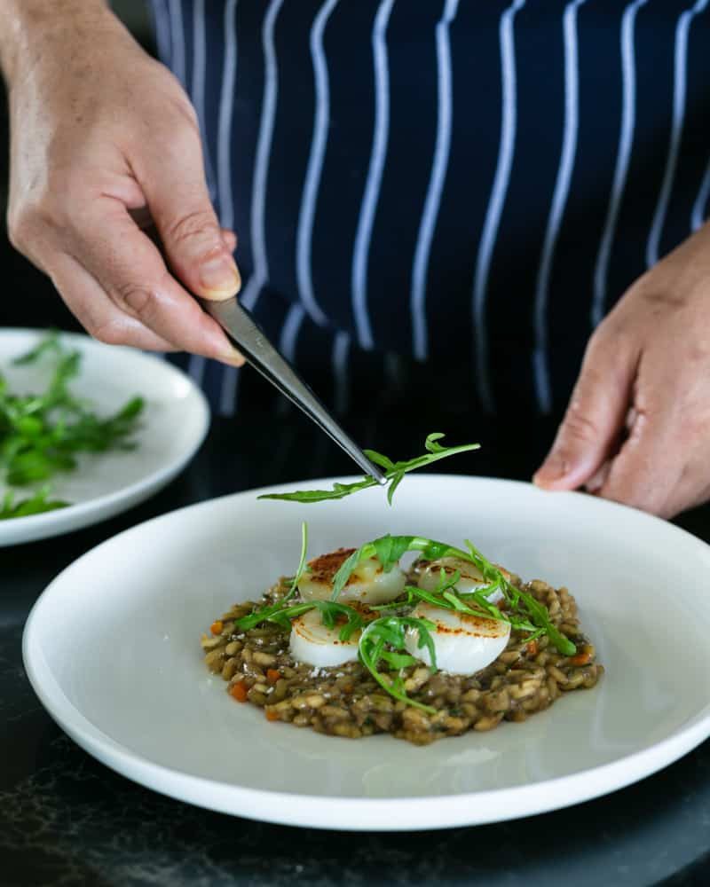 Arugula leaves placed on cooked scallops on top of the risotto