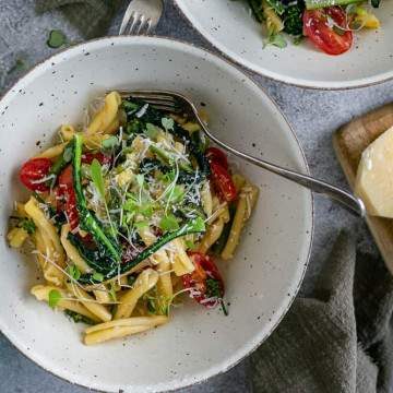 two bowls of Casarecce Pasta with Asparagus, Kale and Garlic with block of parmesan on the side