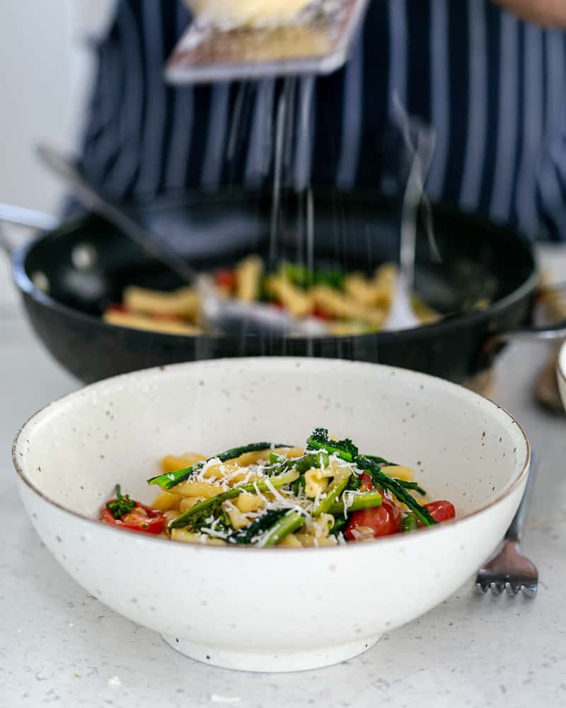 Grating parmesan on top of freshly cooked Casarecce dish with Asparagus, Kale and Garlic in a bowl