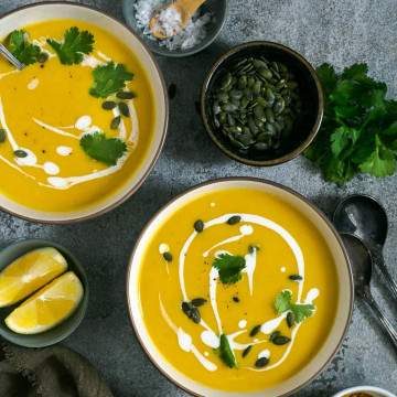 Two bowls of pumpkin soup garnished with pepitas, fresh coriander and coconut milk
