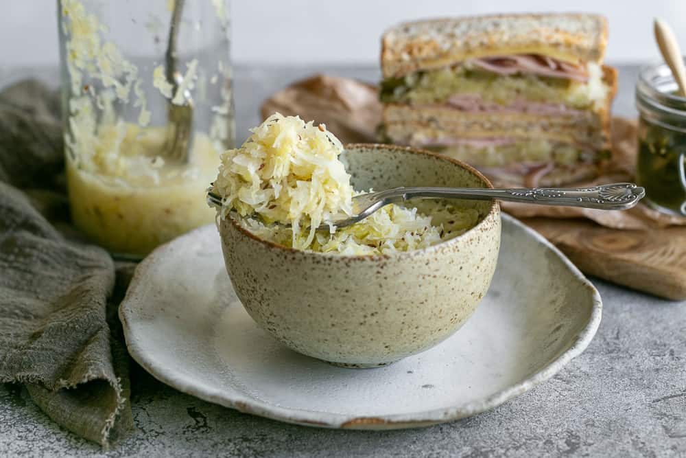 Fermented Sauerkraut served in a ceramic bowl with a fork on top showing a scoop of sauerkraut