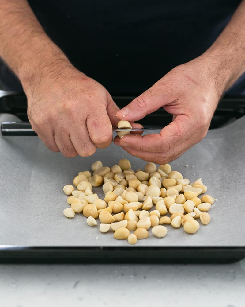 Halving the whole macadamia nuts with a knife before oven roasting them