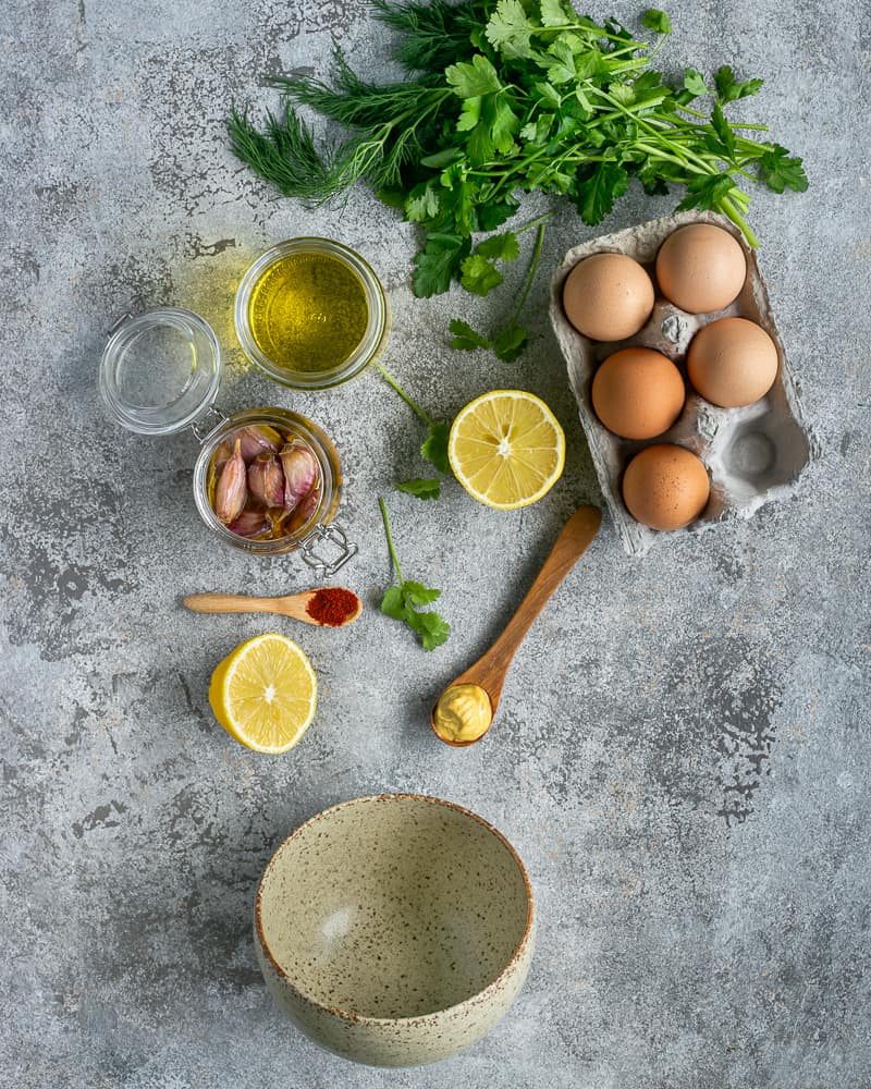 Ingredients for making Confit garlic and herb aioli sauce.  Lemon, mustard. paprika, confit garlic, eggs, fresh herbs like coriander, dill and parsley, grape seed oil