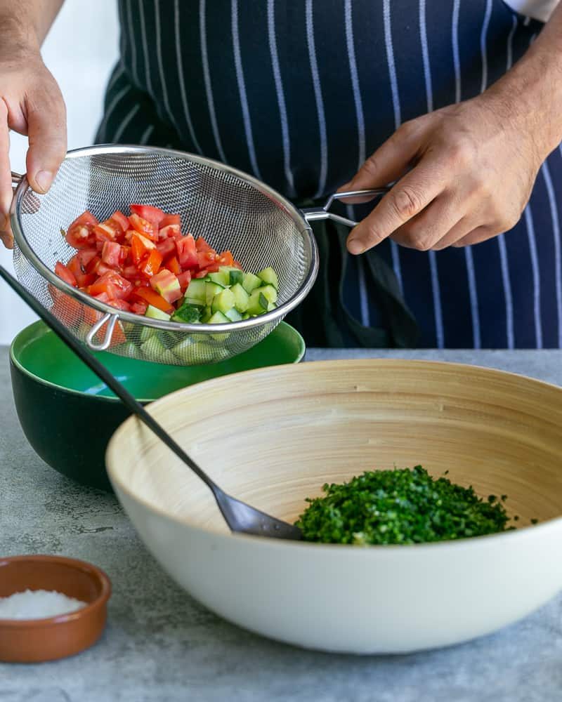 Adding chopped tomatoes and cucumbers to bowl with chopped parsley