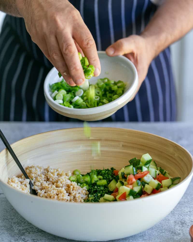 Adding chopped spring onions to bowl with parsley and chopped tomatoes and cucumbers and bulgar