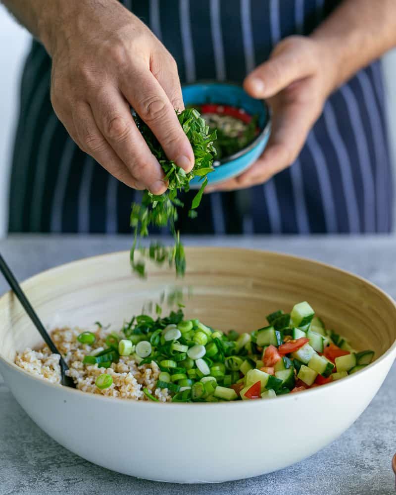 Adding chopped mint to bowl with chopped parsley, tomatoes and cucumbers, bulgar and spring onions