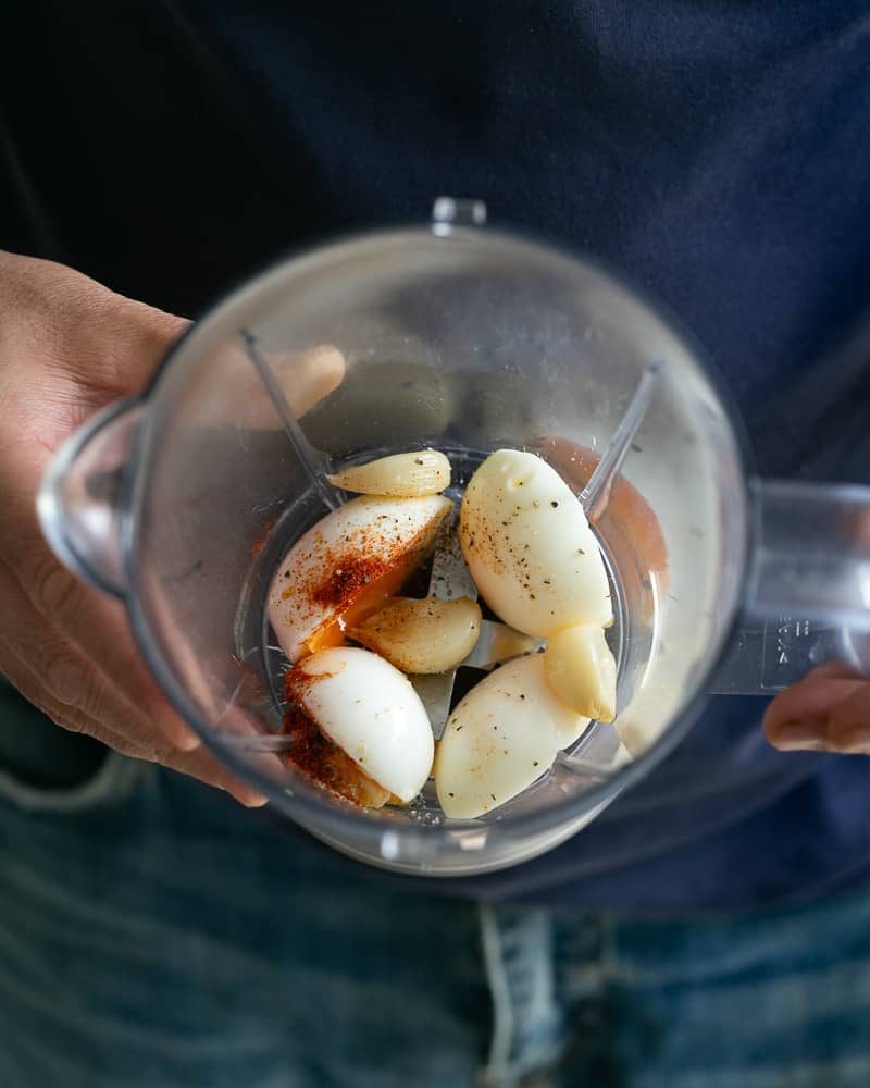 Showing Soft boiled eggs, confit garlic, Mustard, lemon juice, paprika, salt and pepper in the blender jar to make aioli sauce