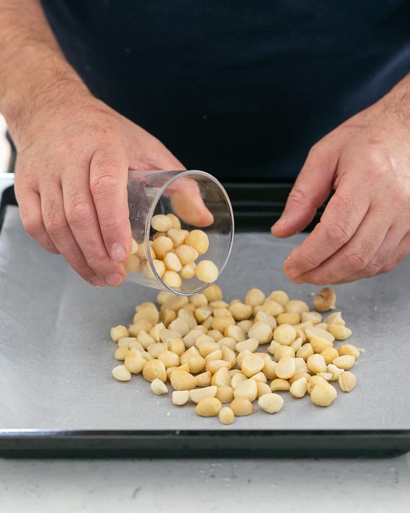 Halved Macadamia nuts spread on baking tray lined with baking paper