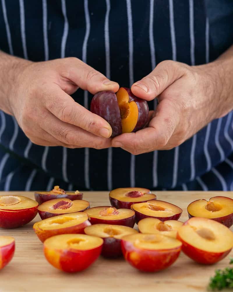 Cutting the halved plums into wedges with a sharp knife on a chopping board