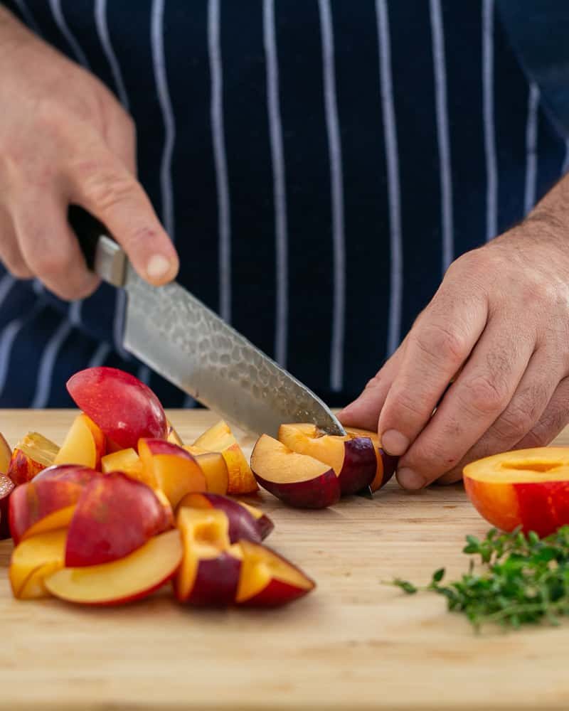 Cutting the halved plums into wedges with a sharp knife on a chopping board