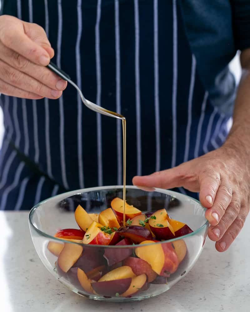 Adding a Teaspoon of vanilla essence to the plum wedges mixed with lemon thyme in the glass bowl for plum tarte tatin