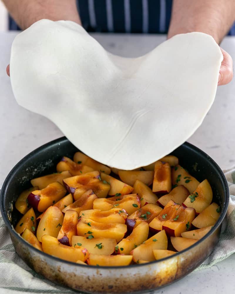 Laying puff pastry sheet on the plums in the caramel sauce plan