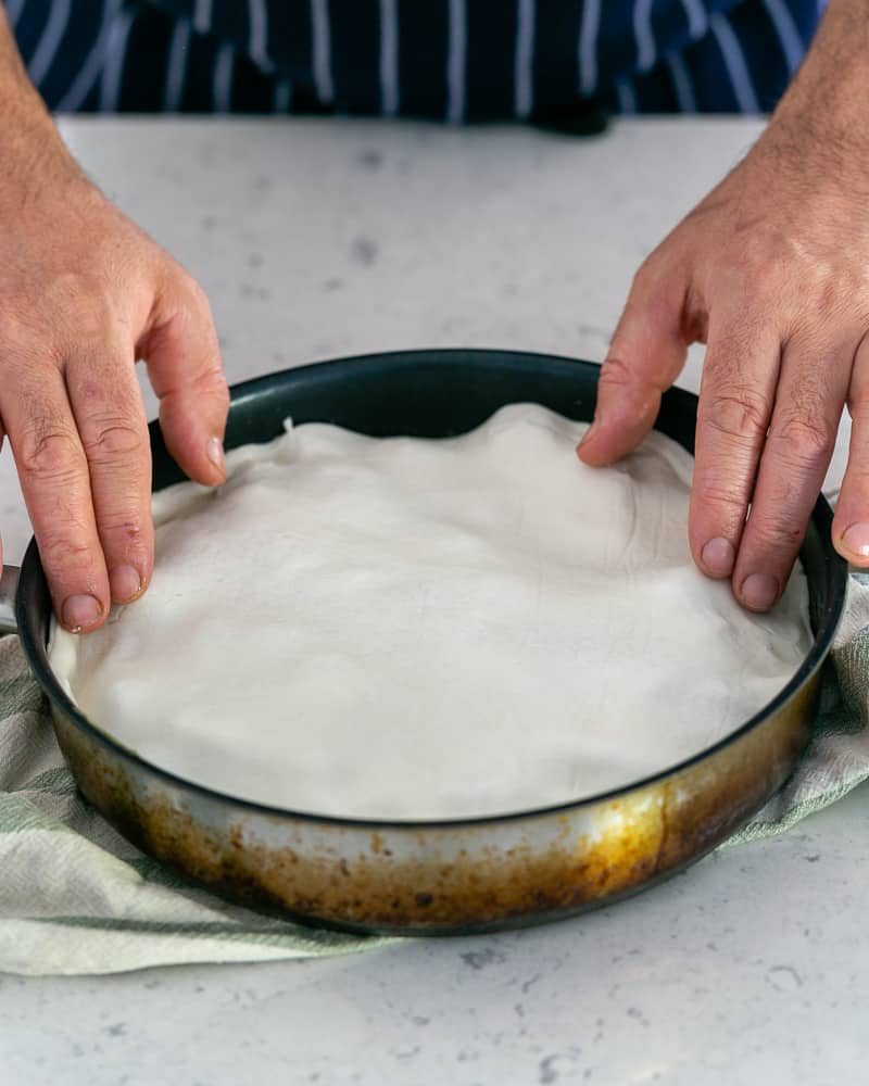 Covering the plums in the caramel sauce in the pan with the puff pastry sheet