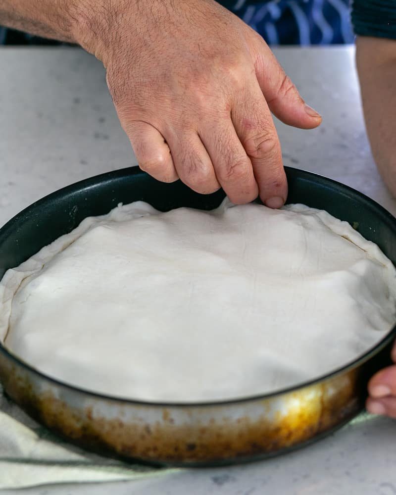 Tucking all sides of the puff pastry sheet in the pan