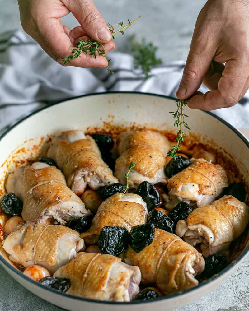 Adding thyme to chciken thighs and prunes in the pan