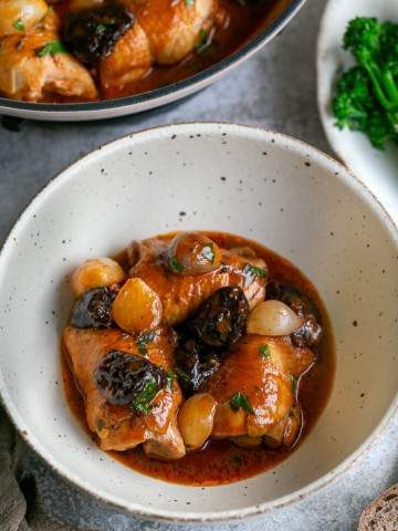 Chicken braised with prunes and shallots served in a bowl with the pan in the background
