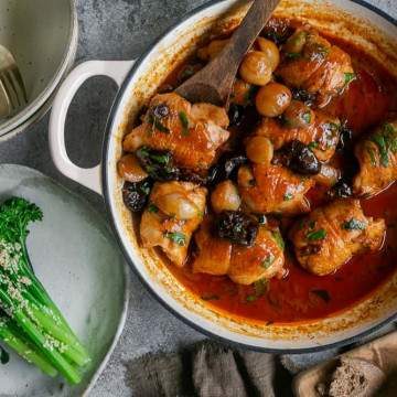 Chicken braised with prunes and shallots in a pan served with a side of broccolini and sourdough bread