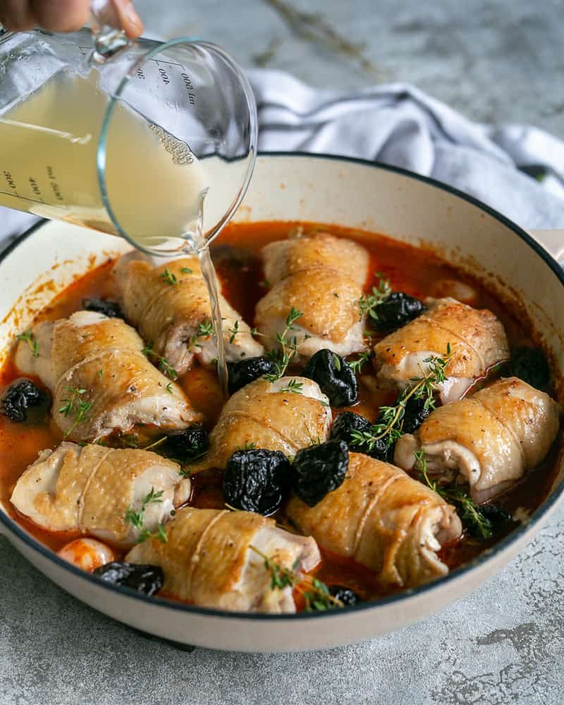 Adding chicken stock to the pan with chicken thighs, prunes and thyme