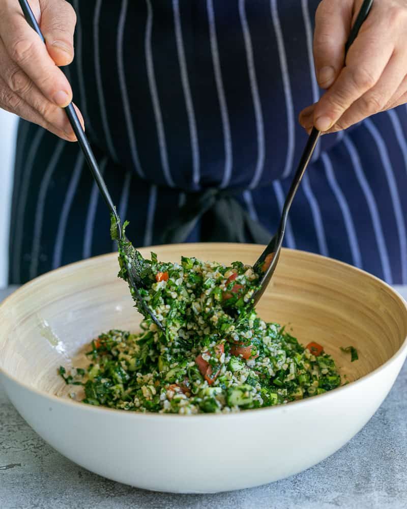 Tossing the tabbouleh salad in a large bowl with salad spoons