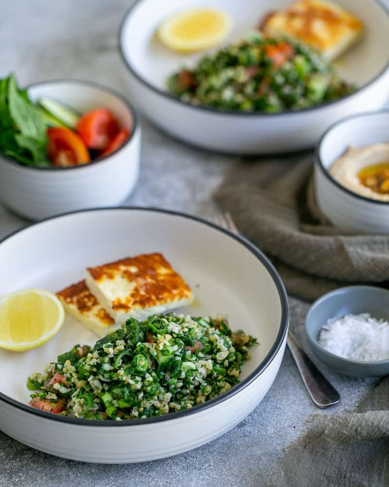 Tabbouleh salad in a whit bowl with two square pieces of pan fried halloumi cheese and half cut lemon