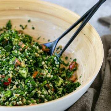 Closeup of tabbouleh salad in a wooden bowl with serving spoons