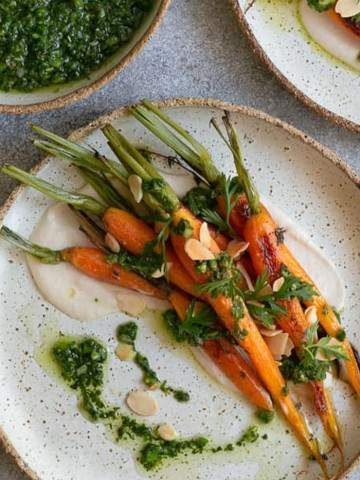 Oven roasted baby carrots with chimichurri beautifully arranged on a ceramic plate