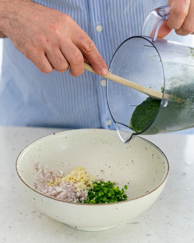 Adding green carrot tops from blender into bowl with other ingredients to make chimichurri sauce