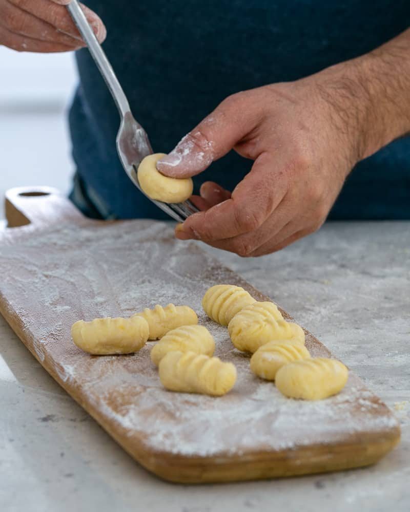 Rolling gnocchi dough balls over a fork to make restaurant style ricotta gnocchi's with tomatoes and olives